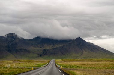 İzlanda 'da bulutlu gökyüzünün altında sisli sıradağlara çıkan boş bir yol..