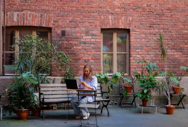 Avluda dizüstü bilgisayarı ve akıllı telefonu olan bir kadın oturuyor. Uzak çalışma kavramı . 