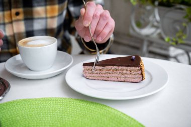 Bir kafede çikolata katmanlı kek ve kapuçino içen kişi, sıcak bir içecek konsepti. 