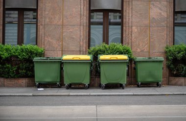 Şehir caddesinde sarı kapaklı yeşil geri dönüşüm kapları, kentsel atık ayrımı kavramı. 