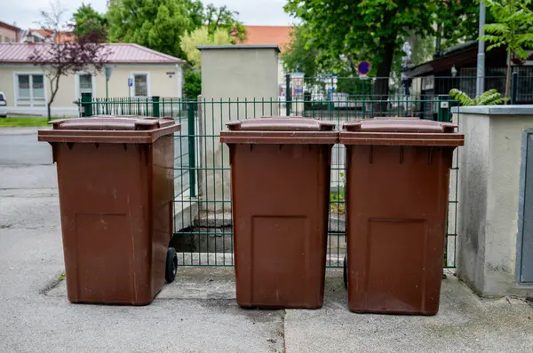 Çitlerin ve konut binalarının yakınındaki caddeye dizilmiş üç kahverengi çöp kutusu.. 