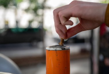 hand pressing cigarette butt against an orange public ashtray pole, concept of anti-littering