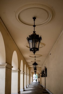 Süslü siyah fenerler klasik sütunlarla bej kemerli bir koridorda asılı..