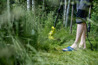 Yazlık bahçede çimleri elektrikli tel budayıcı ile buduyor..
