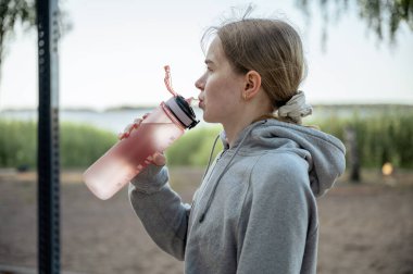 Yaz parkında spor yaptıktan sonra su içen genç bir kadın.. 