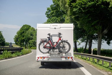 Arka rafa monte edilmiş iki elektrikli bisikletle manzaralı yolda giden bir karavanın arka görüntüsü.. 