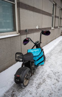 Helsinki, Finlandiya 13 Şubat 2025. Karlı caddede park etmiş Wolt yiyecek çantasıyla elektrikli scooter.
