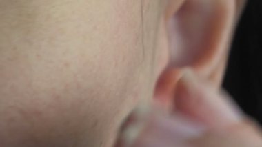 Kız kulağına beyaz bir kablosuz kulaklık takıyor. Kadın kulağı, yakın plan. Makro video. Yüksek kalite 4k görüntü