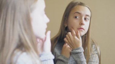 Aynada endişeyle incelenen genç bir kızın portresi yüzünde bir sivilce. Genç bir kız yüzüne sivilce sıkmaya çalışıyor. Gençlerin cilt sorunları. Yüksek kalite 4k görüntü