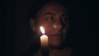Karanlık bir odada elinde mumla beyaz bir kadın etrafına bakar ve mumu üfler. Yüksek kalite 4k görüntü
