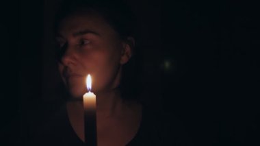 Karanlık bir odada elinde mumla beyaz bir kadın etrafına bakar ve mumu üfler. Yüksek kalite 4k görüntü