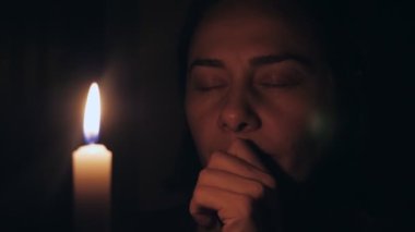 Beyaz bir kadın yanan bir mumun önünde gözleri kapalı dua eder. Kız elleriyle dudaklarına dokundu ve kurtuluş için dua etti. Yüksek kalite 4k görüntü