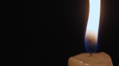 Karanlık bir odada yanan bir mum, mumun alevi etraftaki boşluğu aydınlatıyor. Mumdan çıkan sarı-beyaz ateş. Yüksek kalite 4k görüntü