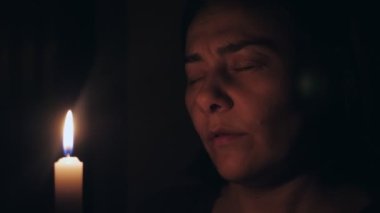 Beyaz bir kadın yanan bir mumun önünde gözleri kapalı dua eder. Kız kurtuluş için bir dua fısıldıyor. Yüksek kalite 4k görüntü