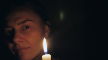 Karanlık bir odada elinde mumla beyaz bir kadın etrafına bakar ve mumu üfler. Yüksek kalite 4k görüntü