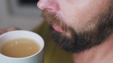 Beyaz sakallı adam mutfakta kahve içiyor. Kısmen gri sakallı bir adamın bardaktan sıcak bir içecek içişi. Yüksek kalite 4k görüntü