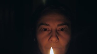 Karanlık bir odada elinde mumla beyaz bir kadın etrafına bakar ve mumu üfler. Yüksek kalite 4k görüntü