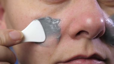 A young woman applies a gray mask to her face after a shower. Spa, skincare, and natural beauty concept at home. A lady takes care of her face with a cosmetic mask. High quality 4k footage