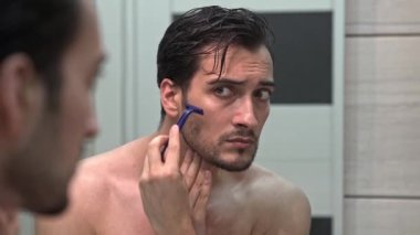 Yakışıklı adam aynaya bakıyor ve banyoda tıraş oluyor.