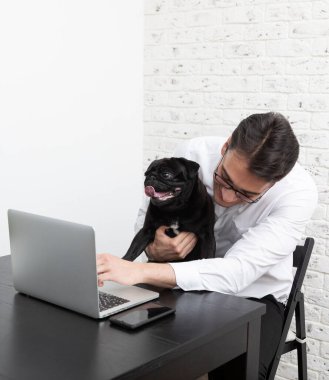 Gülümseyen iş adamı ve sevimli köpeği evde dizüstü bilgisayarla çalışıyor. Uzak çalışma ve arkadaşlık kavramları