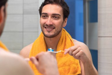 Yakışıklı adam dişlerini fırçalıyor ve banyodaki aynaya bakıyor.