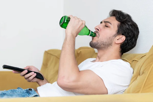 英俊的男人躺在沙发上看电视 喝啤酒 — 图库照片
