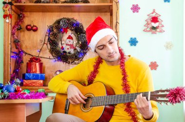 Noel Baba şapkalı genç yakışıklı adam gitar çalıyor ve Noel 'i kutluyor.