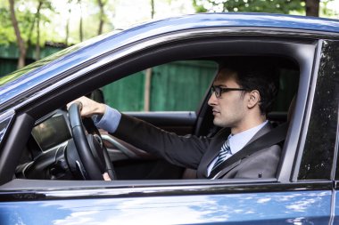 Siyah takım elbiseli yakışıklı bir işadamı lüks bir araba kullanıyor.