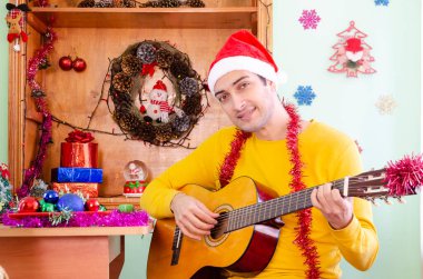 Noel Baba şapkalı genç adam gitar çalıyor ve Noel 'i kutluyor.