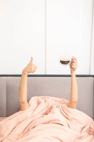 女性手捧着一杯热咖啡躺在床上 喝咖啡和醒悟的概念 — 图库照片