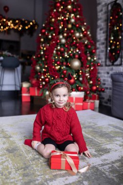 Harika bir tatil zamanı, dekoratif ve şenlikli Noel ağacının yakınında yerde oynayan sevimli küçük kız.