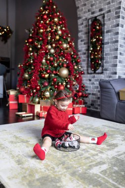 Harika bir tatil zamanı, dekoratif ve şenlikli Noel ağacının yakınında yerde oynayan sevimli küçük kız.