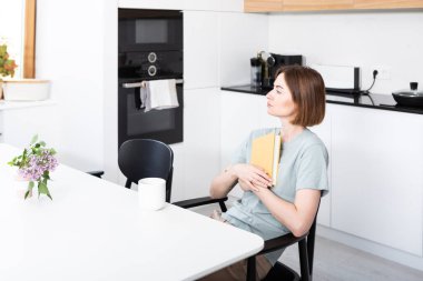 Düşünceli genç bayan mutfakta oturup ilginç kitaplar okuyor.