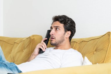 Şok olmuş bir adam kanepede oturuyor ve evde televizyon izliyor.