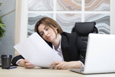 Elinde belgelerle modern ofiste çalışan siyah takım elbiseli ciddi bir iş kadını.