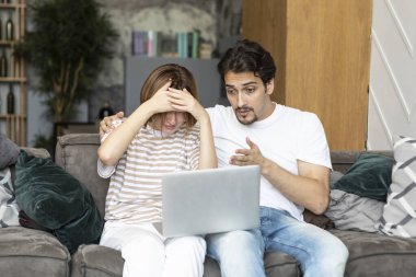 Oturma odasındaki kanepede oturan ve dizüstü bilgisayarda ilginç oyunlar izleyen genç ve neşeli bir çift.