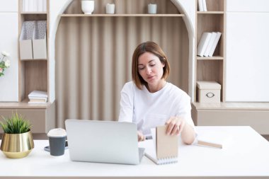 Genç bir kız öğrenci evdeki masada oturuyor ve yeni bir akademik yıla hazırlanıyor. Eğitim ve çevrimiçi eğitim kavramı