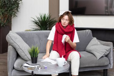 Kanepede oturup kendini tedavi eden grip kadın yüzünden acı çekiyor.