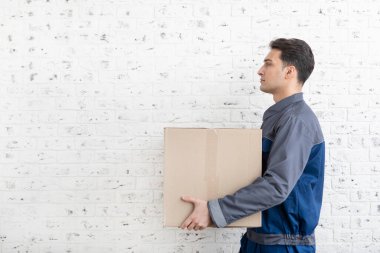 Beyaz tuğlalı arka planda taşınan servis kutusunun yanında duran kendinden emin bir erkek.