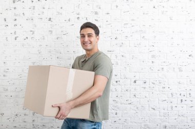 Yakışıklı adam beyaz tuğla duvarın önünde büyük ve ağır bir kutu taşıyor.