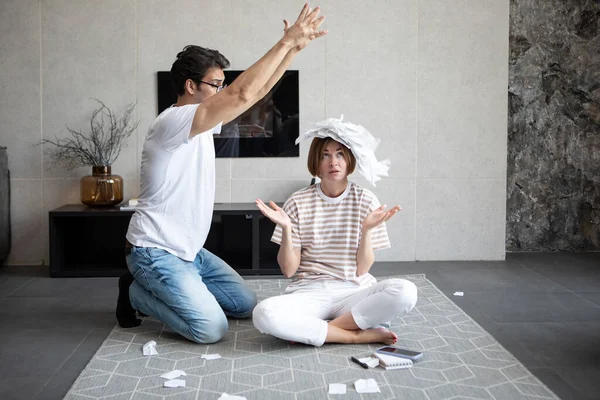 Shocked and depressed married couple sitting on the floor and demonstrating many bills, stressed and confused by calculate expense from invoice or bills, have no money to pay mortgage or loan