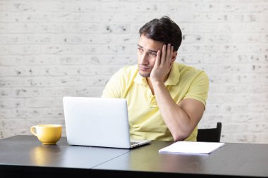 Genç yakışıklı adam evde dizüstü bilgisayarla çalışıyor. Uzaklık çalışması ve çevrimiçi eğitim kavramı