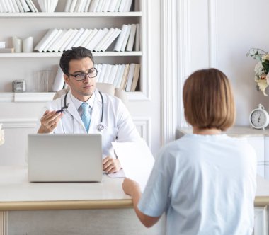 Beyaz önlüklü yakışıklı doktor, modern iş yerinde kadın hasta kabul ediyor.