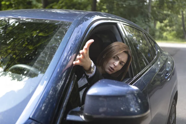 Nervous business woman driving and peeps out of the window of her luxury car. Discontented woman in black suit standing in traffic jam and looking out of her car and demonstrating her displeasure
