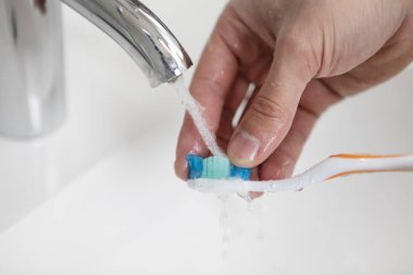 Diş fırçası kullandıktan sonra adamın diş fırçasını yıkarkenki fotoğrafını kapat.