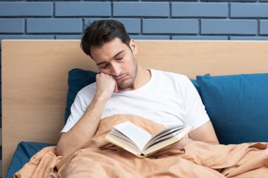 Yorgun adam yatakta kitap okurken uyuyakaldı.