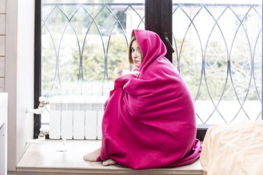 Kadın evde donuyor ve radyatörün yanında oturuyor. Donmuş kız ısıtma sistemine yakın ısınıyor. Benzin ve diğer kamu harcamaları için yüksek fiyatlar