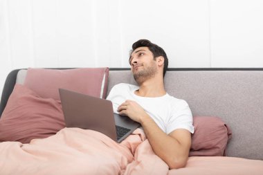Evde dizüstü bilgisayarla çalışırken yatakta uyuyan tembel genç yakışıklı adam.