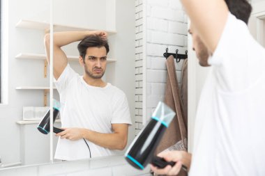 Adam aşırı terliyor ve koltukaltını banyoda aynanın önünde saç kurutma makinesiyle kurutmaya çalışıyor.