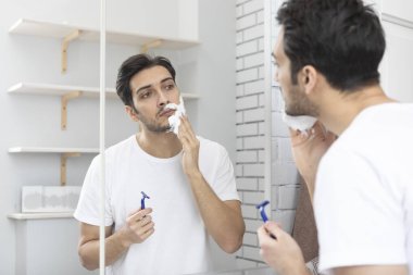 Yakışıklı adam aynaya bakıyor ve banyoda tıraş oluyor.